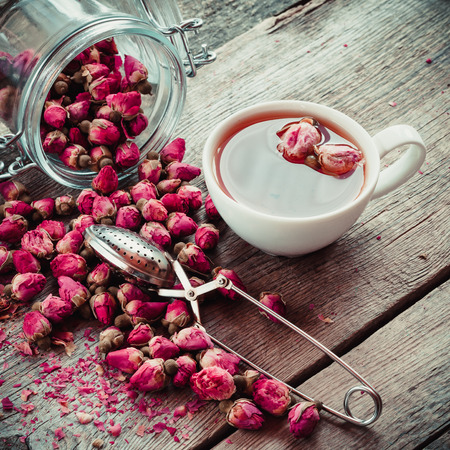 Dry rose flowers, tea cup, strainer and glass jar with rose buds. Selective focus. Retro styled photo.の写真素材
