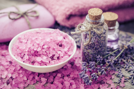 Aromatic sea salt, bottle of dry lavender, essential oil and lavender flowers. Bar of homemade soaps and towel on background.  Selective focus.の写真素材