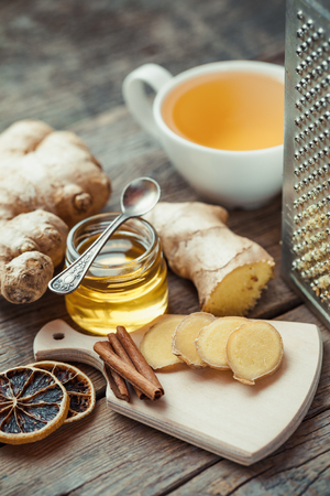Ginger on cutting board, jar of honey, tea cup and grater on kitchen table. Selective focus.の写真素材