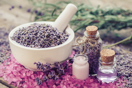 Dry lavender in mortar, aromatic pink sea salt, cream, bottles of essential oil and lavender flowers. Selective focus.の写真素材