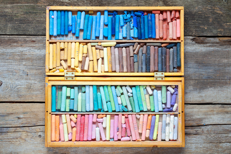Multicolored art pastel crayons in open wooden artist box on table, top view.の写真素材