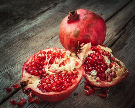 Ripe pomegranate slice and whole red garnet fruit on table. Selective focus. Retro styled.の写真素材