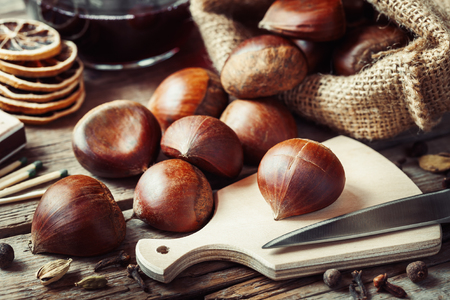 Chestnuts ready to cooking and mulled wine with spices on rustic kitchen tableの写真素材