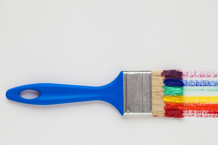 Paintbrush with blue handle and multicolor rainbow brush strokes on white artist canvasの写真素材