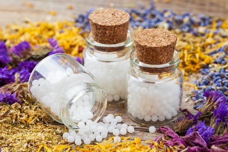 Bottles of homeopathy globules and dry healthy herbs on table. Selective focus.の写真素材
