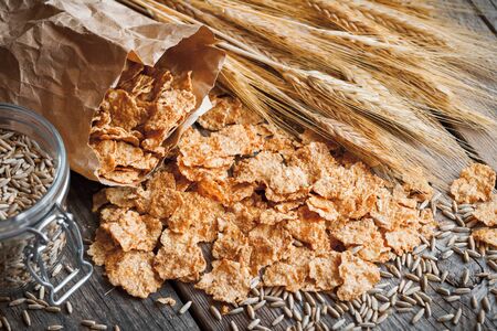 Cereal wheat flakes, spikes and rye grain on old rustic wooden table. Retro toned.の写真素材