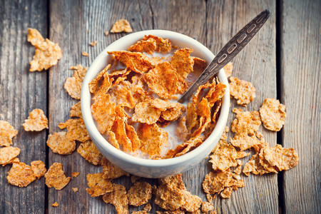 Breakfast cereal wheat flakes in bowl with milk on wooden table