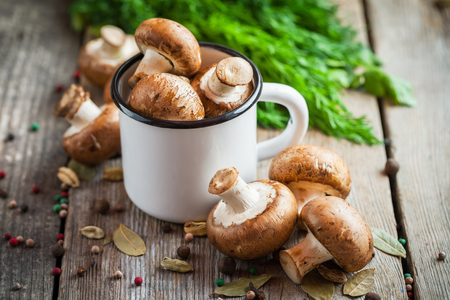 Mushrooms in white enameled mug, dill and spices on wooden table.の写真素材