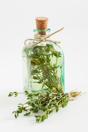 Transparent bottle of thyme essential oil or infusion and healing herbs bunch closeup on white. Selective focus.の写真素材
