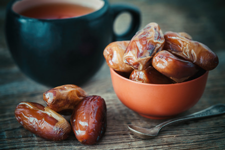 Dates fruits in bowl and tea cup on background. Retro toned photo.の写真素材