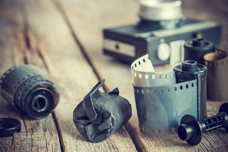 Old photo film rolls and cassette on old wooden desk, vintage camera on background. Retro toned.の写真素材