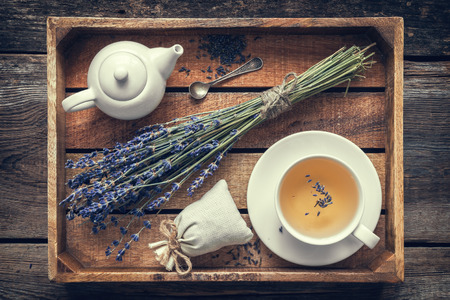 Bunch of lavender flowers, healthy tea in cup, teapot and sachets filled with dried lavender in wooden tray. Retro toned. Top view. Flat lay.の写真素材