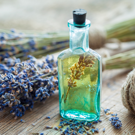 Bottle of essential oil and bunch of lavender flowers on table. の写真素材
