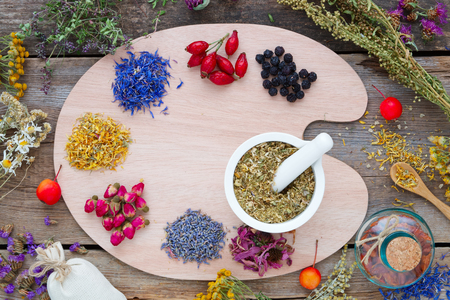 Healing herbs on wooden palette, mortar, tincture bottle and medicinal herbs on old wooden board. Top view. Herbal medicine concept.の写真素材