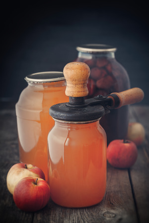 Glass jar of juice, apples and retro can lid closing machine for canning.の写真素材