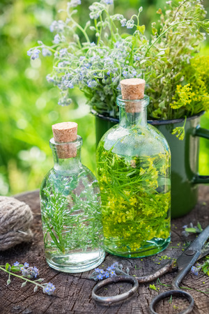 Bottles of tincture or infusion of healing herbs, medicinal herbs in green enameled mug on old stump outdoors. Herbal medicine concept.の写真素材