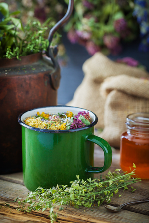 Enameled mug of healing herbs, old tea kettle, honey jar and medicinal plants for healthy herbal tea. Herbal medicine.の写真素材