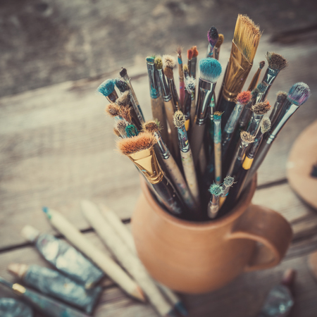Paintbrushes in a jug from potters clay, wooden palette and paint tubes.の写真素材