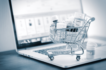 Mini shopping cart full of homeopathic remedies on laptop background. Homeopathy and internet online shopping concept. Black and white stylized.の写真素材