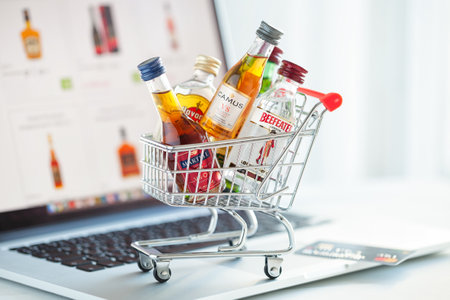 Minsk, Belarus - January 16, 2018: Illustrative editorial photo of mini shopping cart full of small alcohol bottles -  Camus and Martell cognacs, Havana club rum, Beefeater gin on laptop background. Minsk, Belarus.のeditorial素材