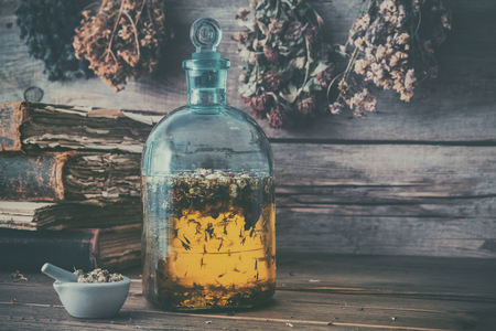 Tincture or potion bottle, old books, mortar and hanging bunches of dry healthy herbs. Herbal medicine. Retro styled.の写真素材