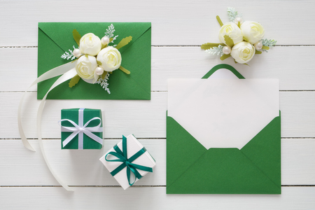 Wedding invitation cards or Valentines Day letters in green envelopes decorated with white rose flowers and two gift boxes.の写真素材
