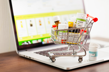 Mini shopping cart full of homeopathic remedies on laptop background. Homeopathy and internet online shopping concept.の写真素材