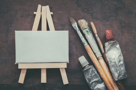 Artist paintbrushes, paint tubes and small easel with canvas closeup. Top view.の写真素材