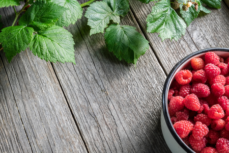 Bowl full of raspberries and leaves on wooden board. Top view. Copy space for text.の写真素材
