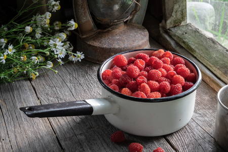 Bowl full of raspberry berries on wooden table in a retro village house.の写真素材