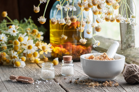 Mortar of dried healing herbs, homeopathic globules, bottle of oil or infusion and bunches of dry chamomile plant. Homeopathy and herbal medicine.の写真素材