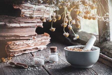Mortar of dried healing herbs, bottles of homeopathic globules, old books and bunch of dry chamomile plant. Homeopathy medicine.の写真素材