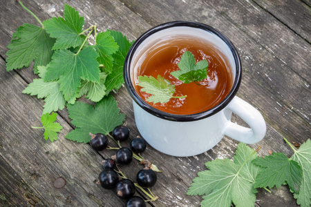 Enameled cup of fruit tea with black currant berries on wooden table outdoors. Top view.の写真素材