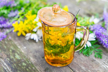 Healthy herbal tea or infusion cup and medicinal herbs bunches on wooden board.の写真素材