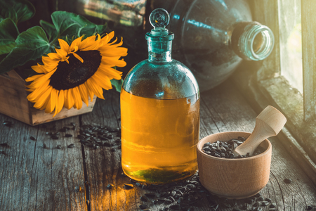Bottle of sunflower oil, wooden mortar of seeds and yellow sunflower on wooden table inside the retro village house.の写真素材