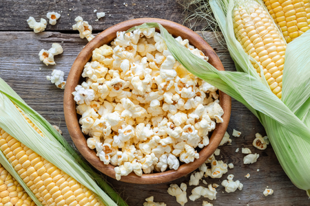 Prepared popcorn in wooden bowl, corncobs on table. Top view.の写真素材