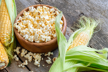Prepared popcorn in wooden bowl, corncobs on wooden table.の写真素材
