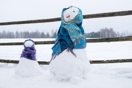 Two cute snowmen wrapped in scarves on snowy field.の写真素材