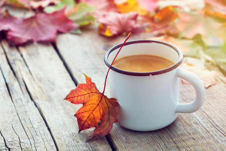Enameled cup of coffee in and fallen maple leaves on wooden board.の写真素材