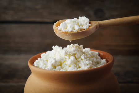 Cottage cheese in rustic vintage clay pot and wooden spoon.の写真素材