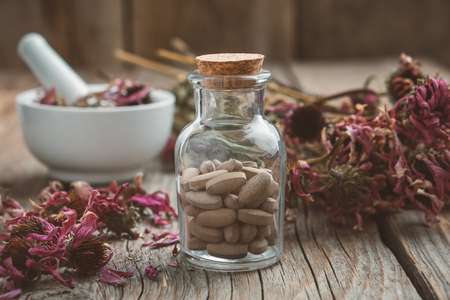 Bottle of herbal pills, mortar of healthy echinacea herbs and dry coneflower bunch on wooden table.の写真素材