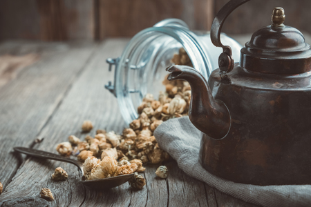 Vintage teapot and glass of dry healthy chamomile buds on wooden table.の写真素材