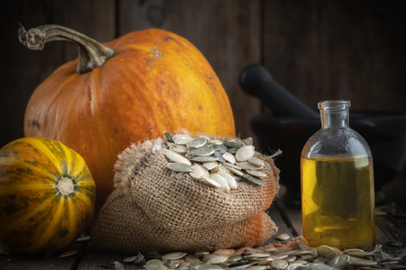 Pumpkin seeds oil bottle, two pumpkins, bag of seeds and mortarの写真素材