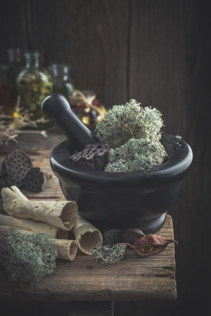Mortar of dried moss and lotus, dry roots, nuts and plants on old table.の写真素材