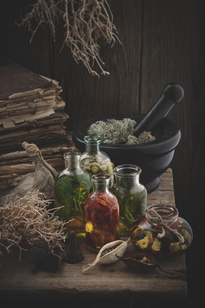 Bottles of essential oil, mortar of dried moss, old books, dry roots, nuts and plants. Herbal medicine.の写真素材