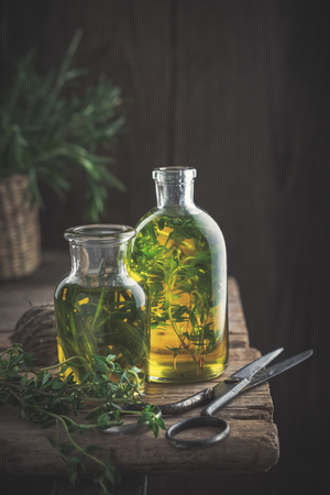 Bottles of thyme and rosemary essential oil or infusion and scissors on old wooden table.の写真素材