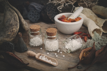 Bottles of homeopathic globules, mortar of dried chili pepper, dry roots, nuts and plants. Homeopathy medicine.の写真素材
