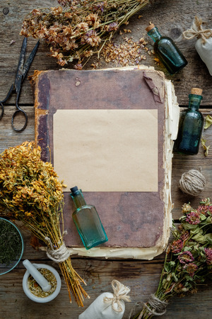 Old antique book, tincture bottles, assortment of bunches of dry medicinal herbs, mortar. Herbal medicine. Top view.の写真素材