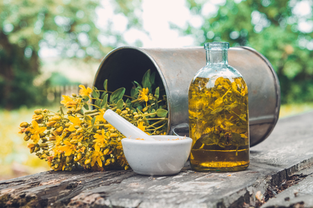 Hypericum - St Johns wort flowers, oil or infusion bottle, mortar and big vintage metal mug of Hypericum flowers on wooden board outdoors.の写真素材
