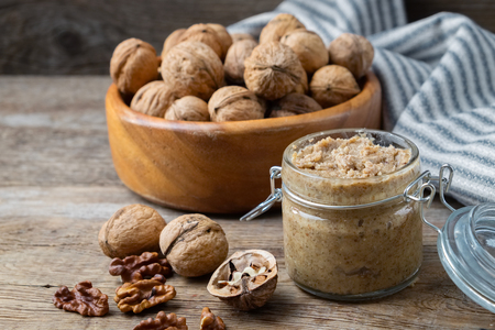 Glass jar of raw organic walnut butter or paste and fresh nuts in bowl on table.の写真素材